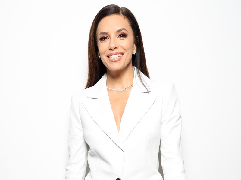 Eva Longoria smiles in white suit against white backdrop