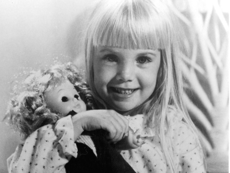 Black and white photo of child actress Heather O'Rourke smiling and holding doll toy