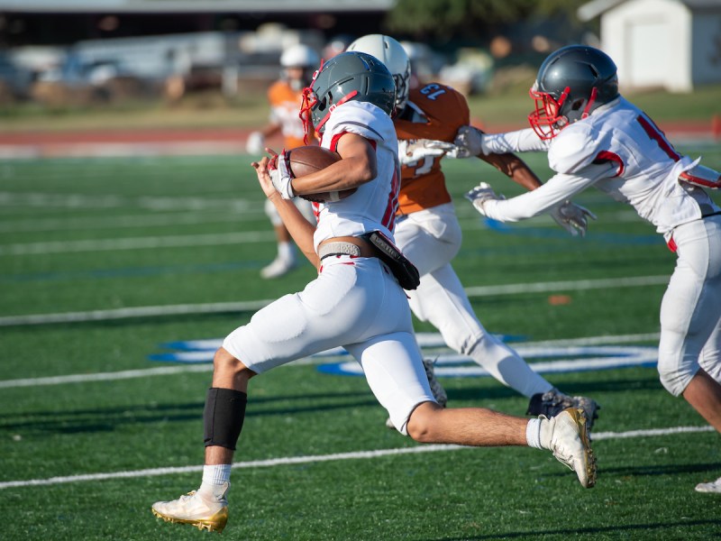 a man in white football uniform running with a football down a field as other players chase him
