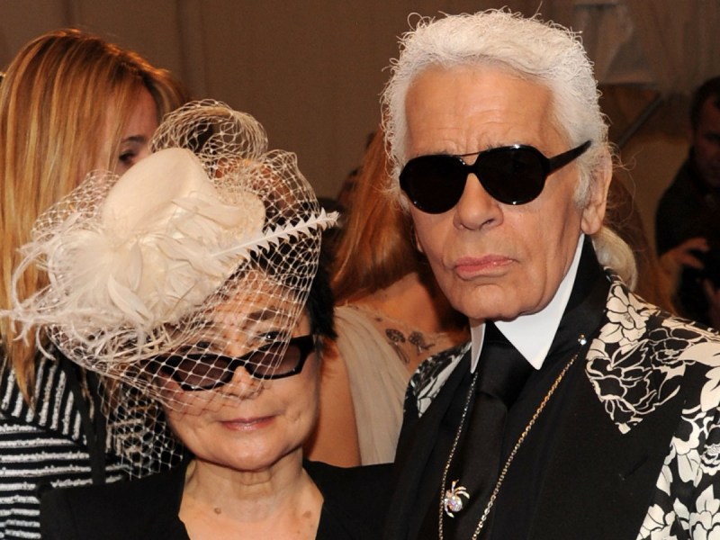 Yoko Ono (L) in white hat and Karl Lagerfeld, who is dressed in black and white with dark sunglasses