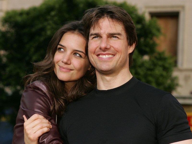 Katie Holmes (L) wrapping her arms around Tom Cruise in an outdoor scape. Both are smiling
