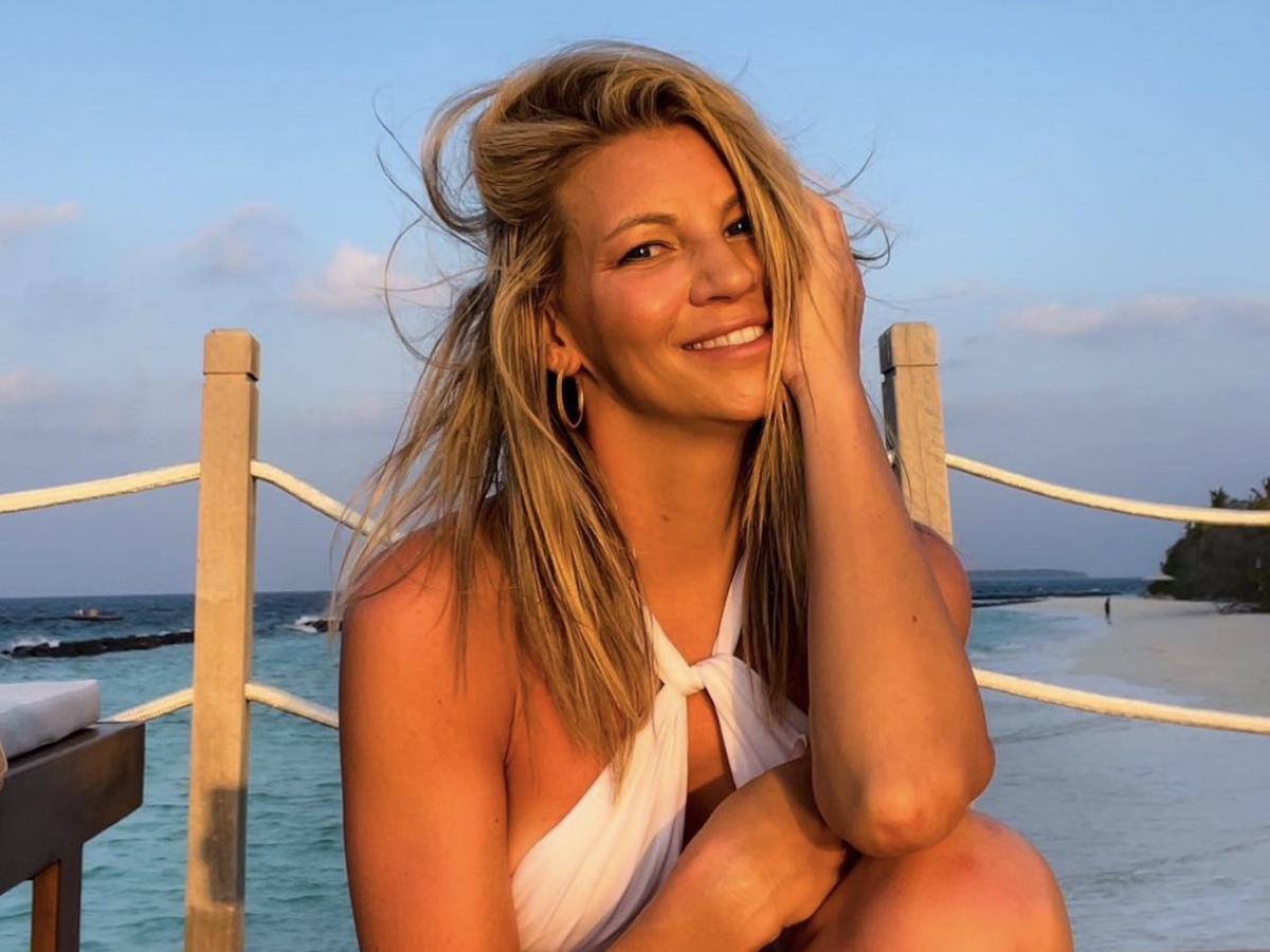 screenshot of Kelly Crump smiling in a white bathing suit on a dock at sunset