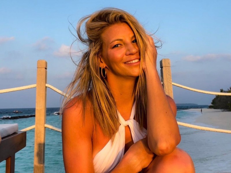screenshot of Kelly Crump smiling in a white bathing suit on a dock at sunset