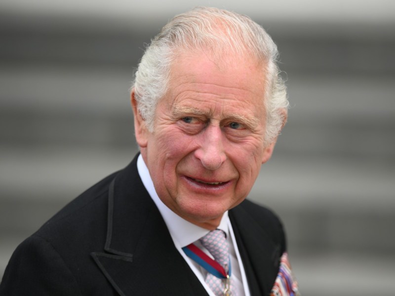 King Charles smiles in closeup photo while wearing a black suit and patterned tie