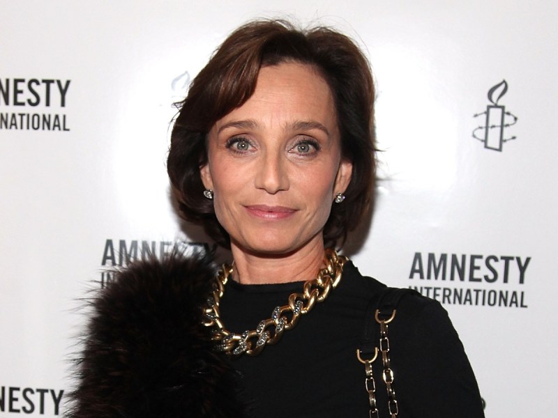 Kristen Scott Thomas smiles in black dress against white backdrop