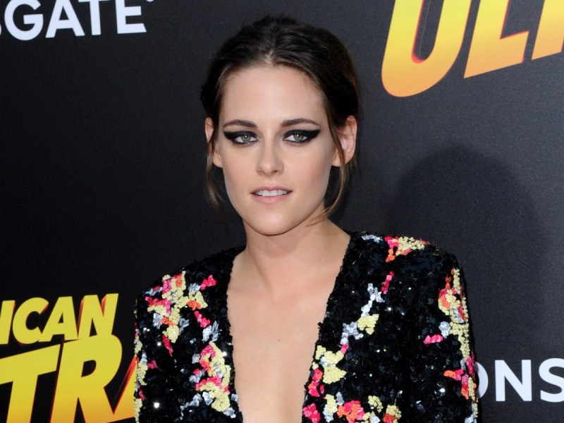 Kristen Stewart smiles in black floral dress against black backdrop