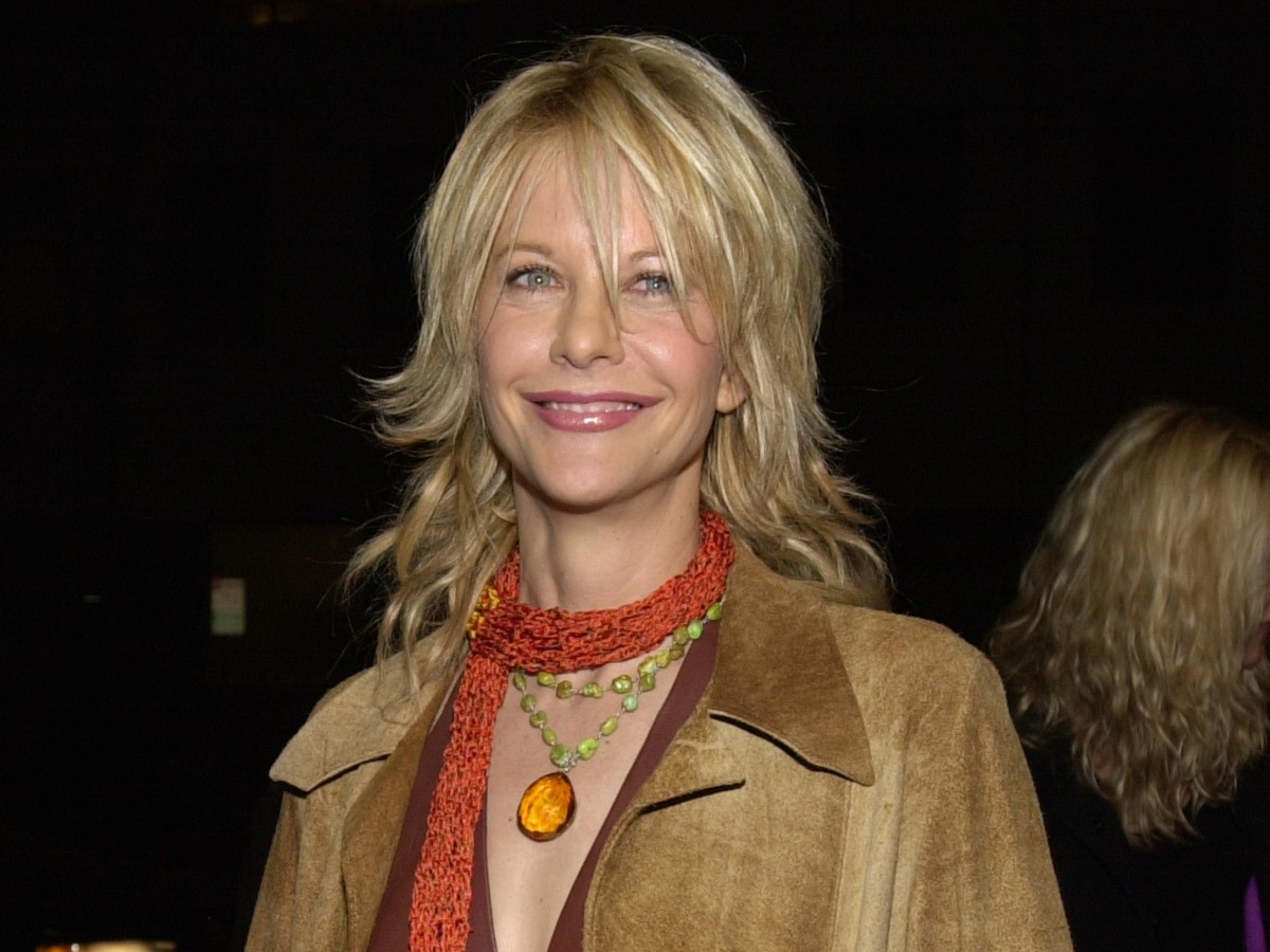 Meg Ryan smiles in orange scarf and tan jacket