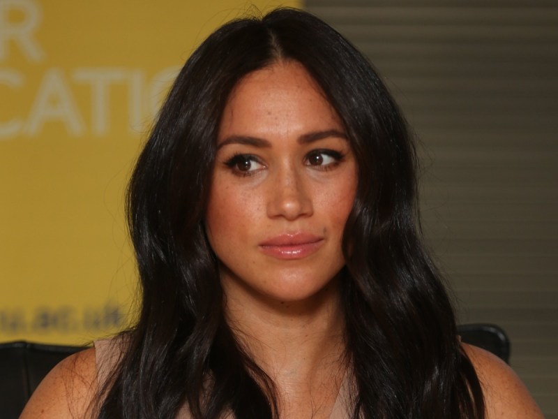 Meghan Markle looks off to the side against yellow backdrop