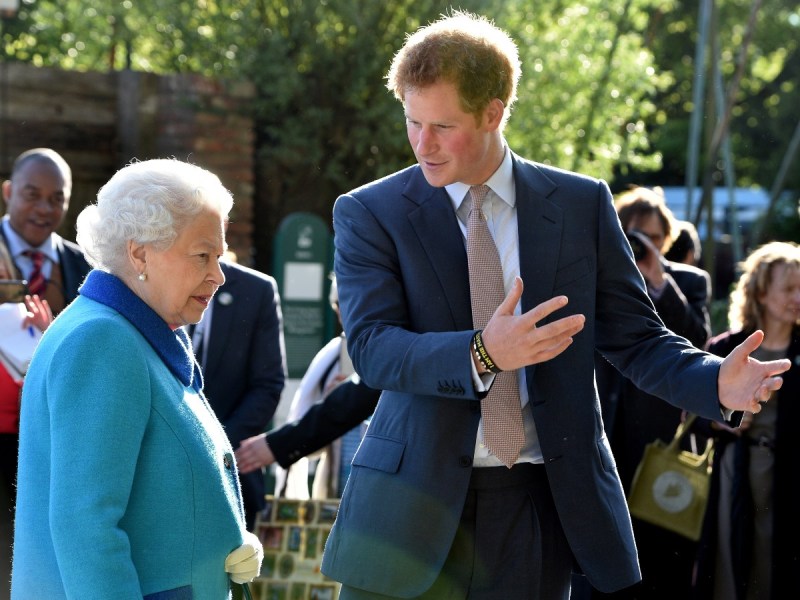 Prince Harry (R) gesturing and talking to Queen Elizabeth, who is following behind him