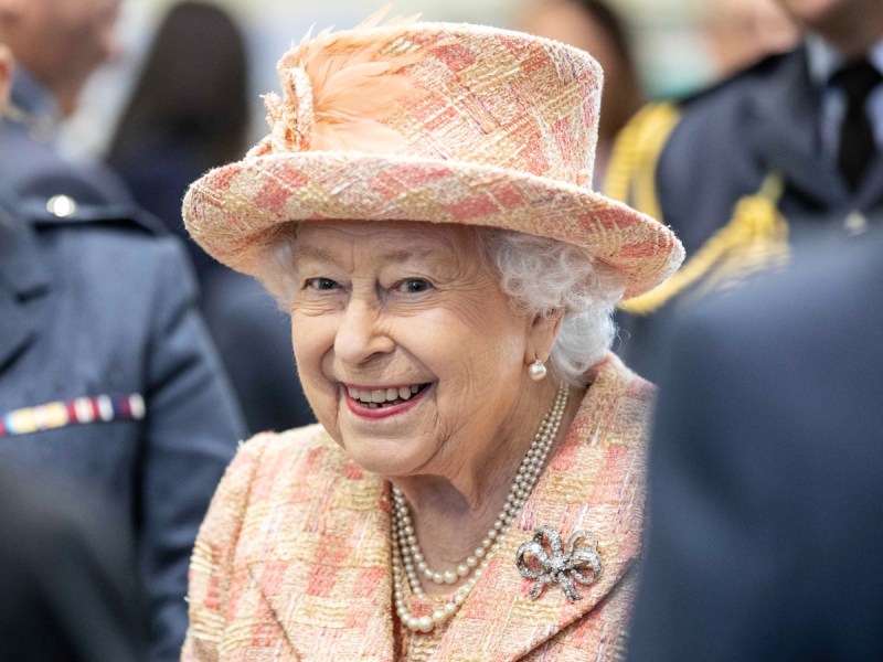 Queen Elizabeth smiles in patterned suit and matching hat
