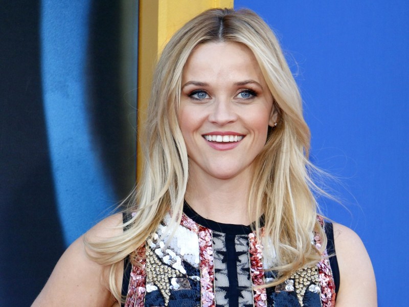 Reese Witherspoon smiles in floral-patterned dress against blue backdrop