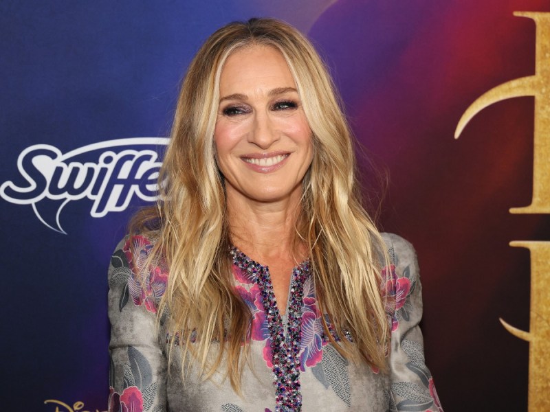 Sarah Jessica Parker smiles in patterned button-down top against purple backdrop