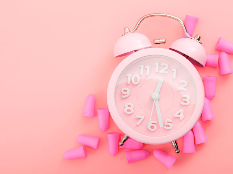 A pink alarm clock and ear plugs representing pink noise.