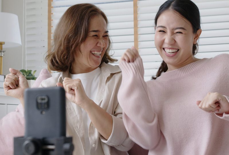 A mom and her teenage daughter dancing and smiling while looking at a mobile device