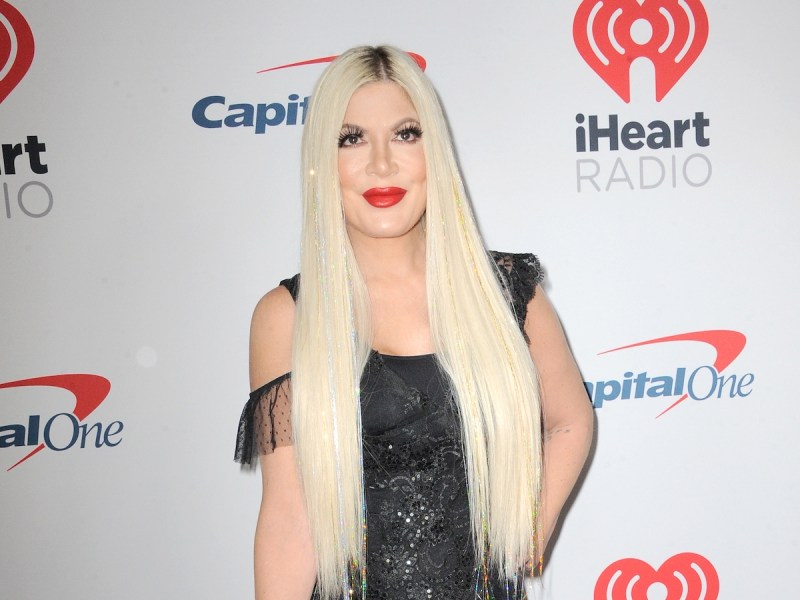 Tori Spelling smiling in a black dress with red lipstick