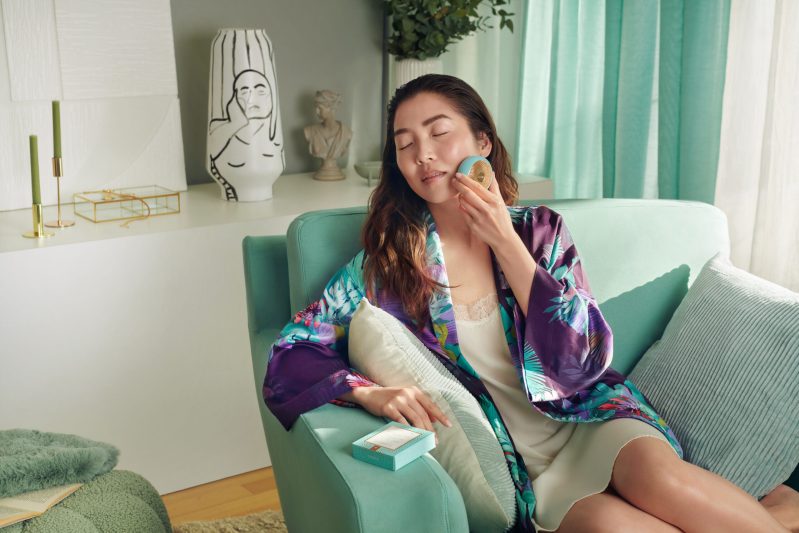 A woman lounges on a sofa using a FOREO UFO 2
