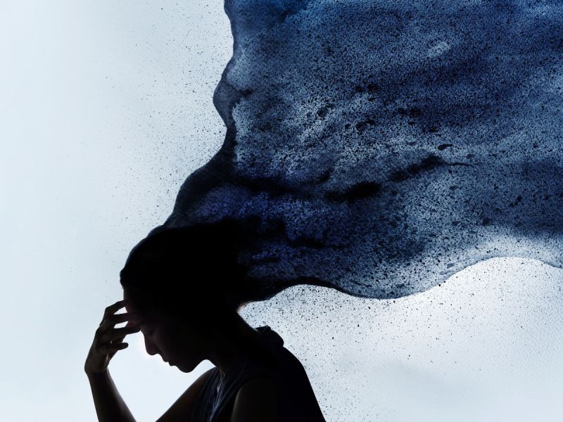 Depressed woman touching forehead with blue cloud billowing out from head