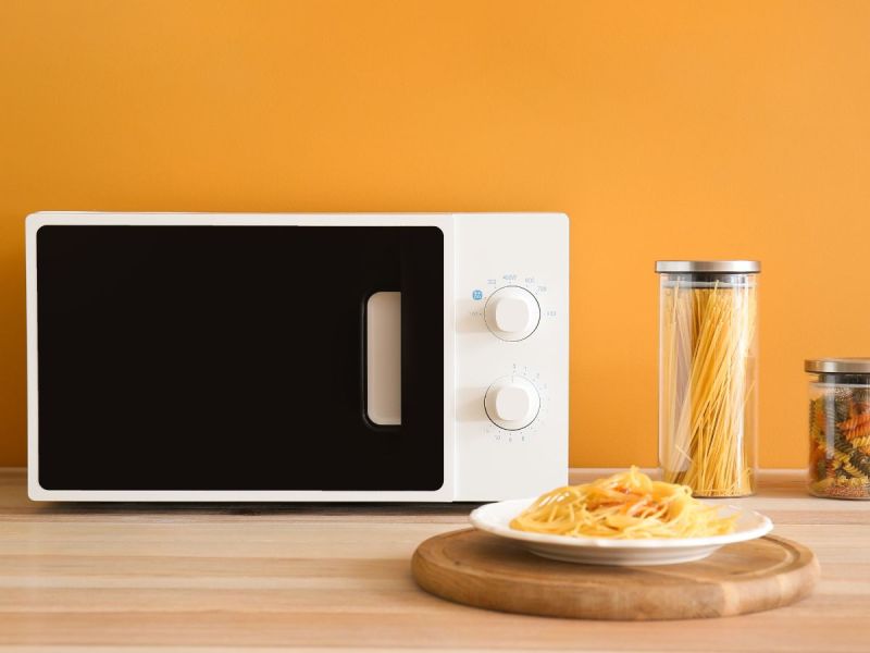 Plate of pasta sitting in front of a microwave and a yellow wall