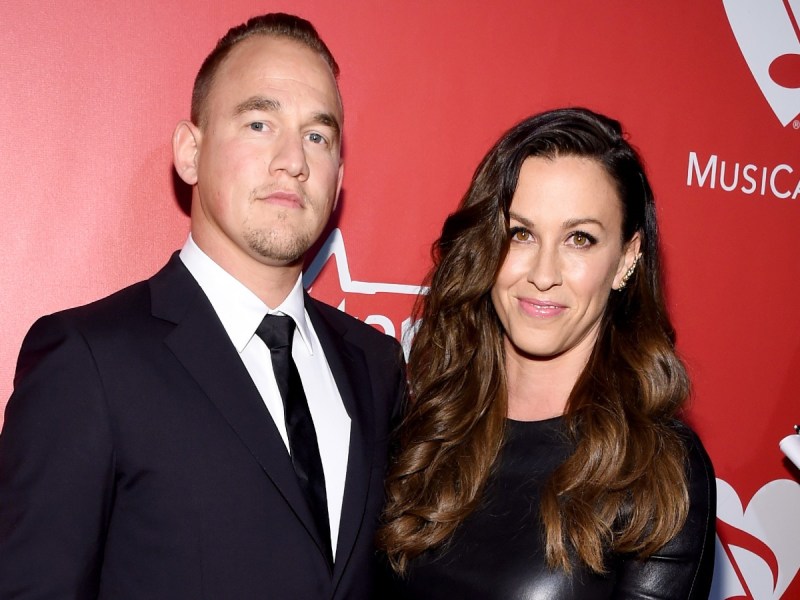 Alanis Morissette (R) and Souleye smiling against red backdrop