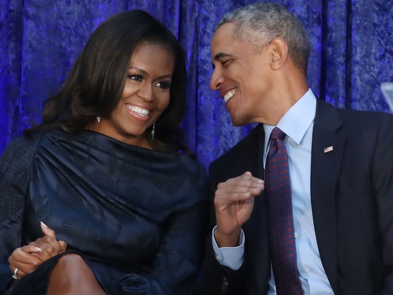 Michelle Obama (L) in blue dress laughing next to Barack Obama