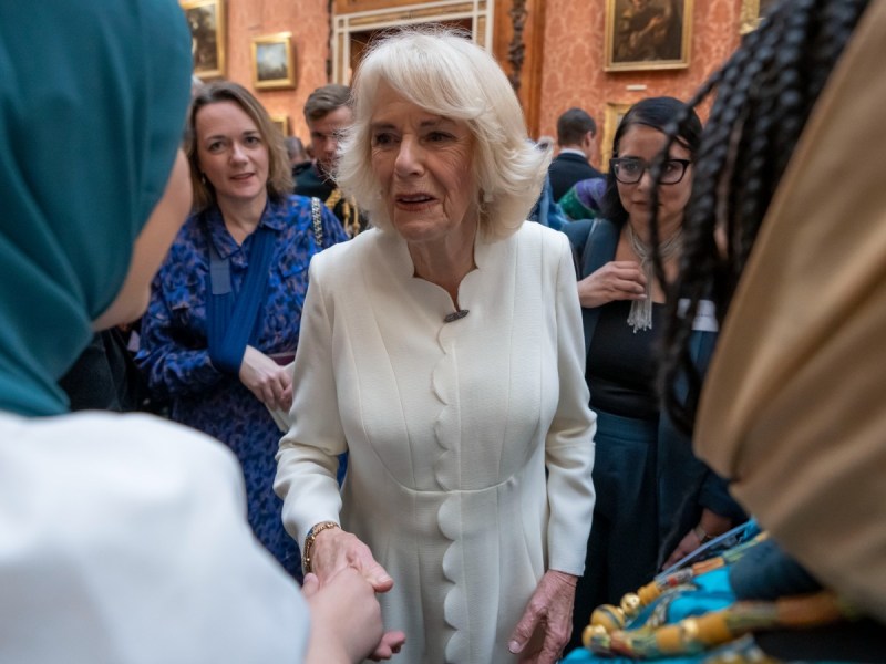 Camilla Parker Bowles shakes hands with a woman wearing a white top and teal hijab