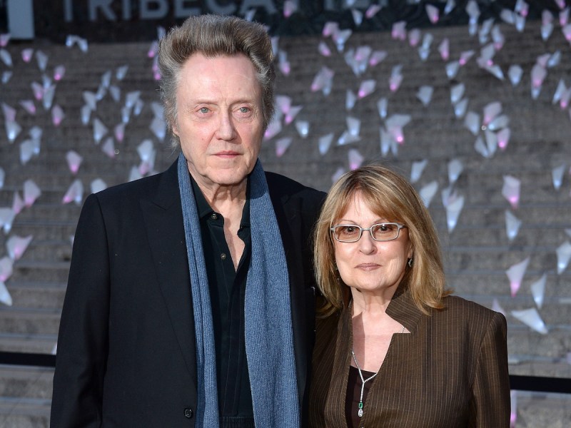 2013 photo of Christopher Walken in a black coat and blue scarf with arm around wife Georgianne Walken in a brown coat