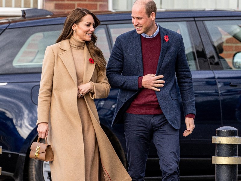 Kate Middleton (L) in tan shirt and coat walking next to Prince William, who is wearing a burgundy sweater with dark blue jacket