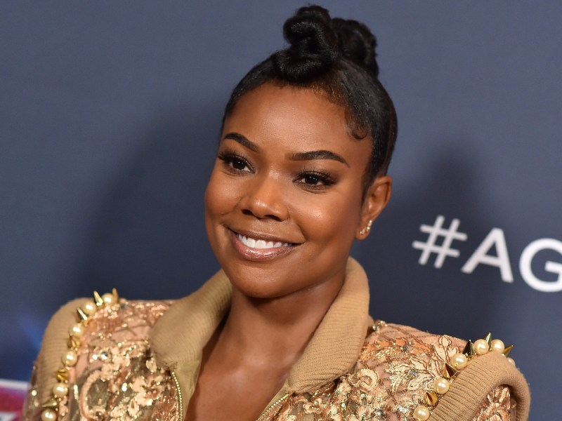 Gabrielle Union smiles with top knot hairstyle and gold blazer