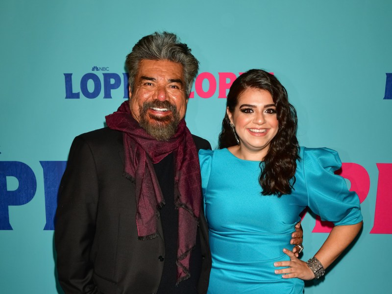 George Lopez smiling in a black jacket and maroon scarf with Mayan Lopez in a blue dress