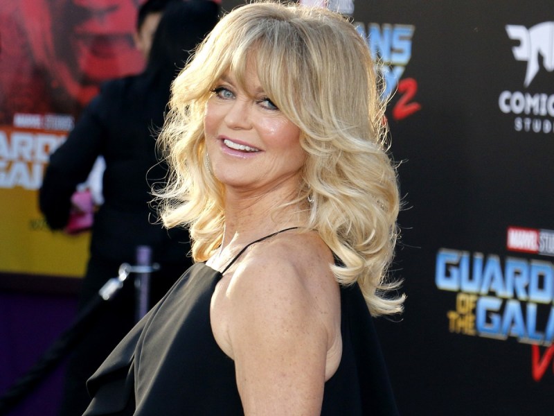 Goldie Hawn smiles in black dress against black backdrop