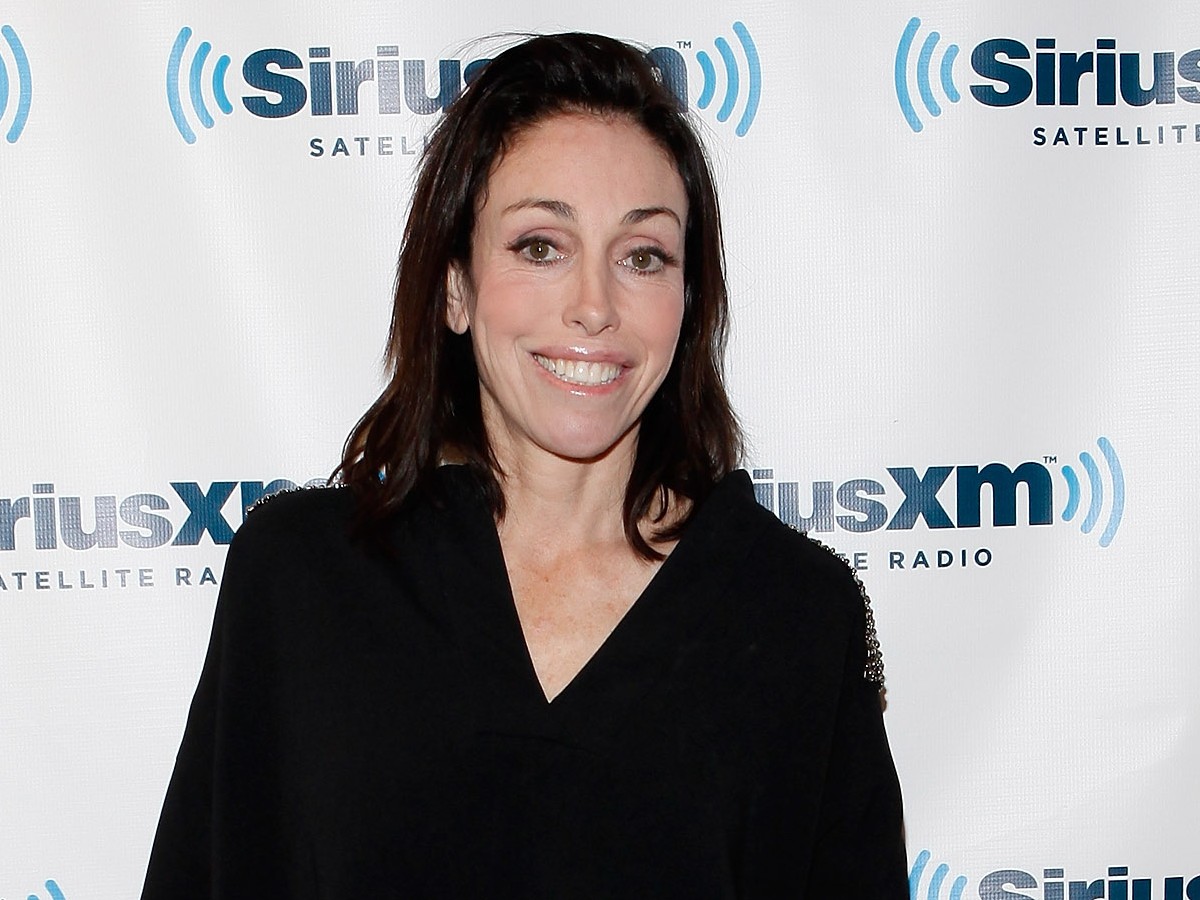 Heidi Fleiss smiles in black top against white backdrop