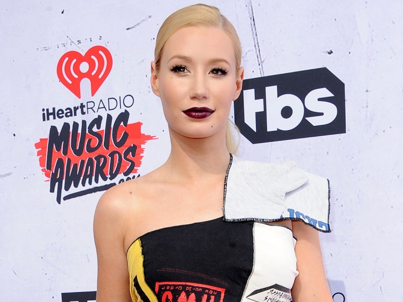 Iggy Azalea smiles in black and white top against white backdrop