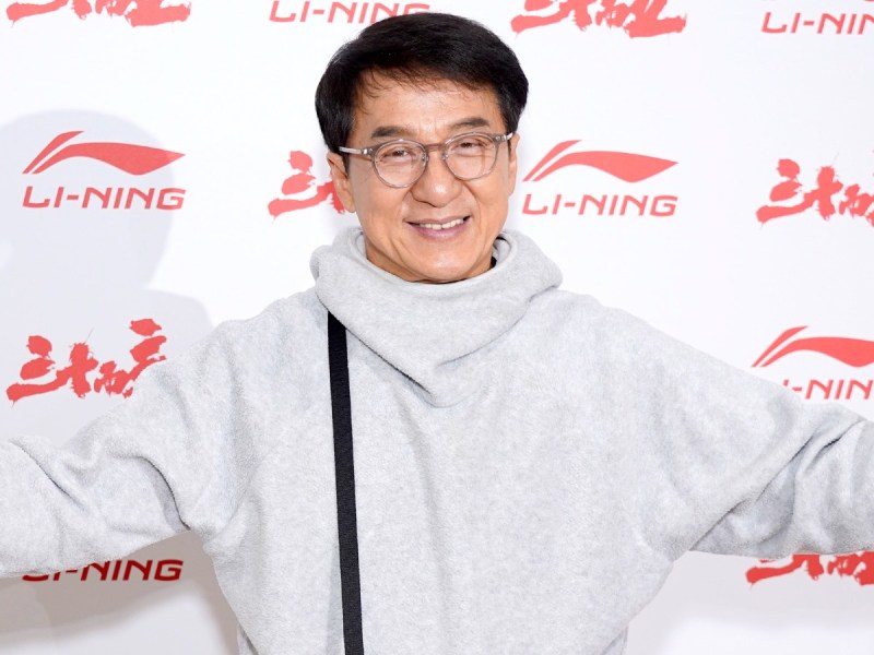 Jackie Chan smiles in light gray hoodie