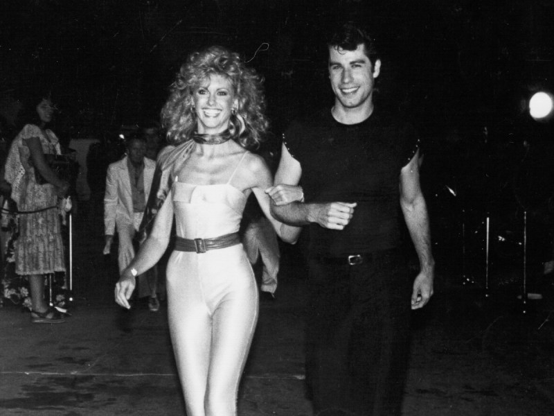 Black and white photo of John Travolta (R) and Olivia Newton John linking arms and walking