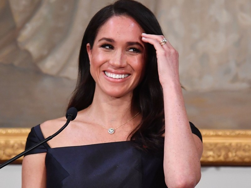 Meghan Markle smiles while brushing back her hair with her hand