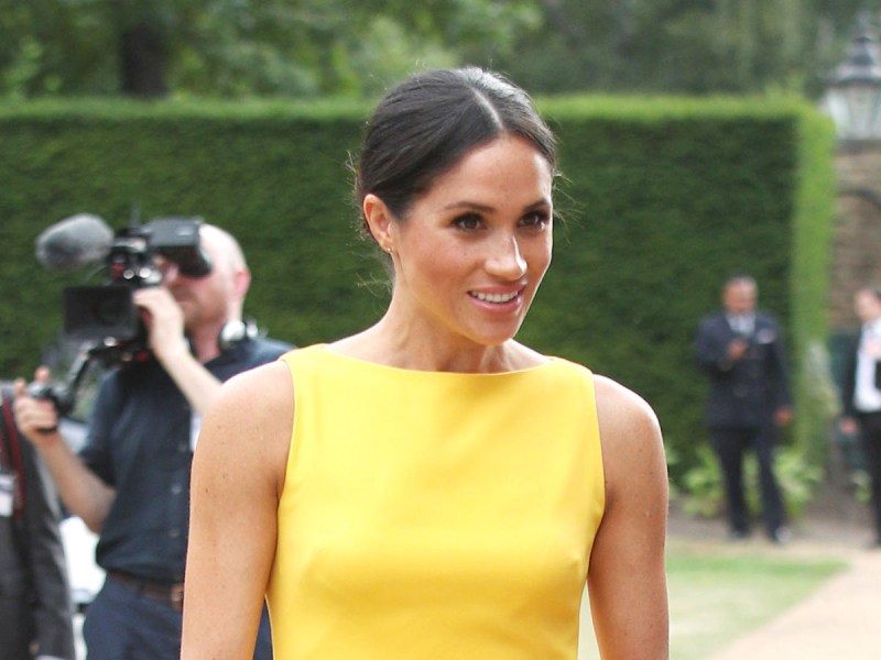 2018 photo of Meghan Markle smiling in a yellow dress outdoors