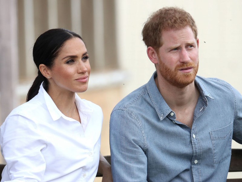 Meghan Markle in white shirt sitting with Prince Harry in a blue shirt