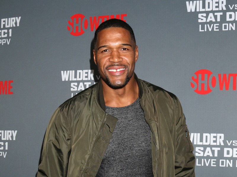 Michael Strahan in a green jacket and grey shirt smiling