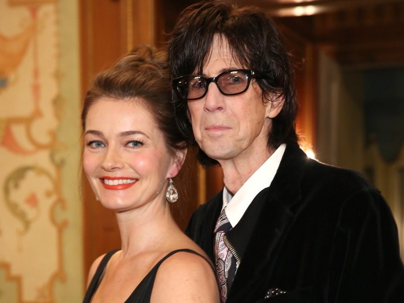 Paulina Porizkova (L) in black gown smiling next to Ric Ocasek, who is wearing a black suit jacket