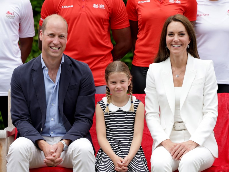 Prince William smiling and sitting with Princess Charlotte and Princess Catherine