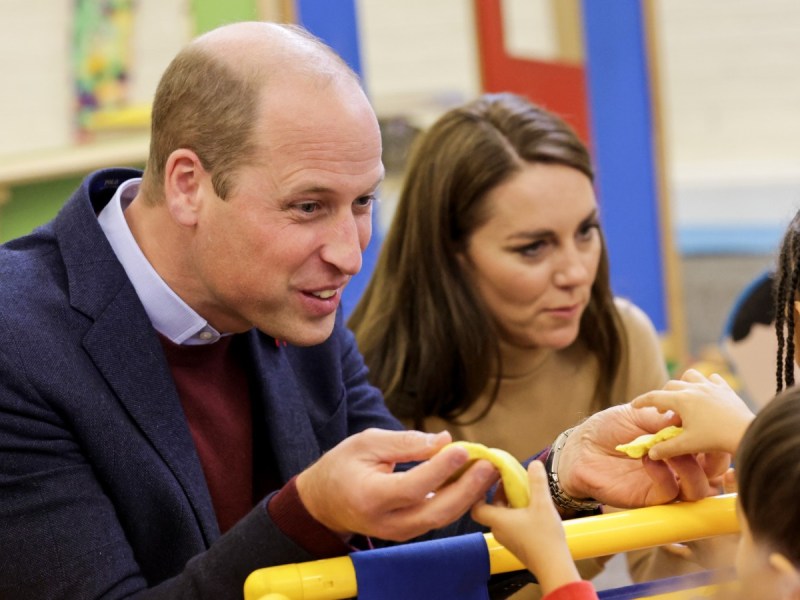 Prince William (L) and Kate Middleton smiling and touching hands with children