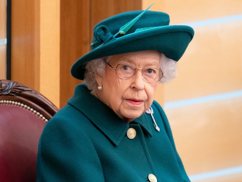 Queen Elizabeth looks at camera in teal jacket and matching hat