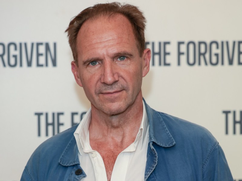 Ralph Fiennes in white dress shirt and denim jacket against off-white backdrop