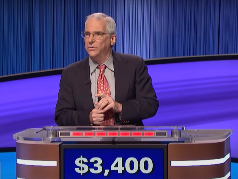 screenshot of Sam Buttrey competing on Jeopardy!, holding his buzzer straight up and down with one hand and placing the index finger of his other hand over the button