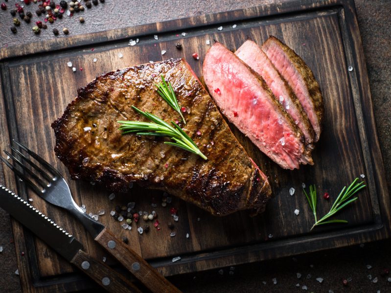 A grilled steak partially sliced on a cutting board