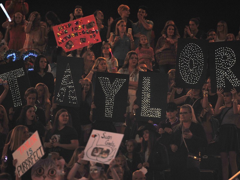 Fans at a Taylor Swift Concert holding up signs praising the singer