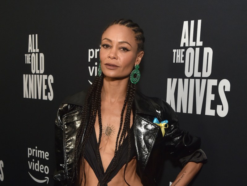 Thandiwe Newton posing in a black strapped outfit with green earrings