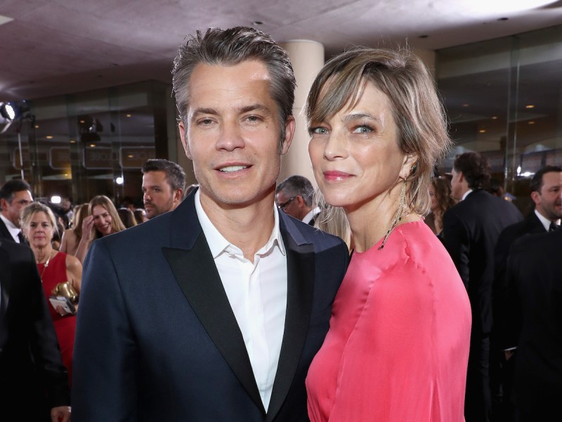 Timothy Olyphant smiling in a navy suit with wife Alexis Knief in a pink dress