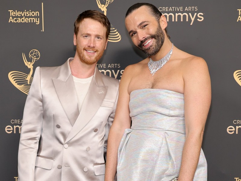Mark Peacock (L) in satin suit standing next to Jonathan Van Ness, who is wearing a strapless silver gown