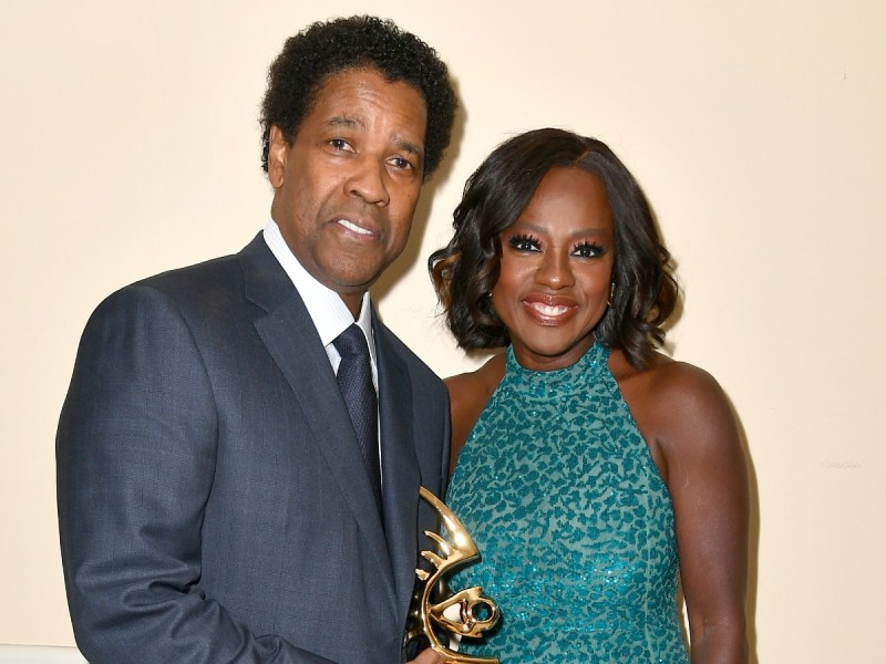 Viola Davis (R) in teal dress smiling next to Denzel Washington, who is wearing a charcoal gray suit